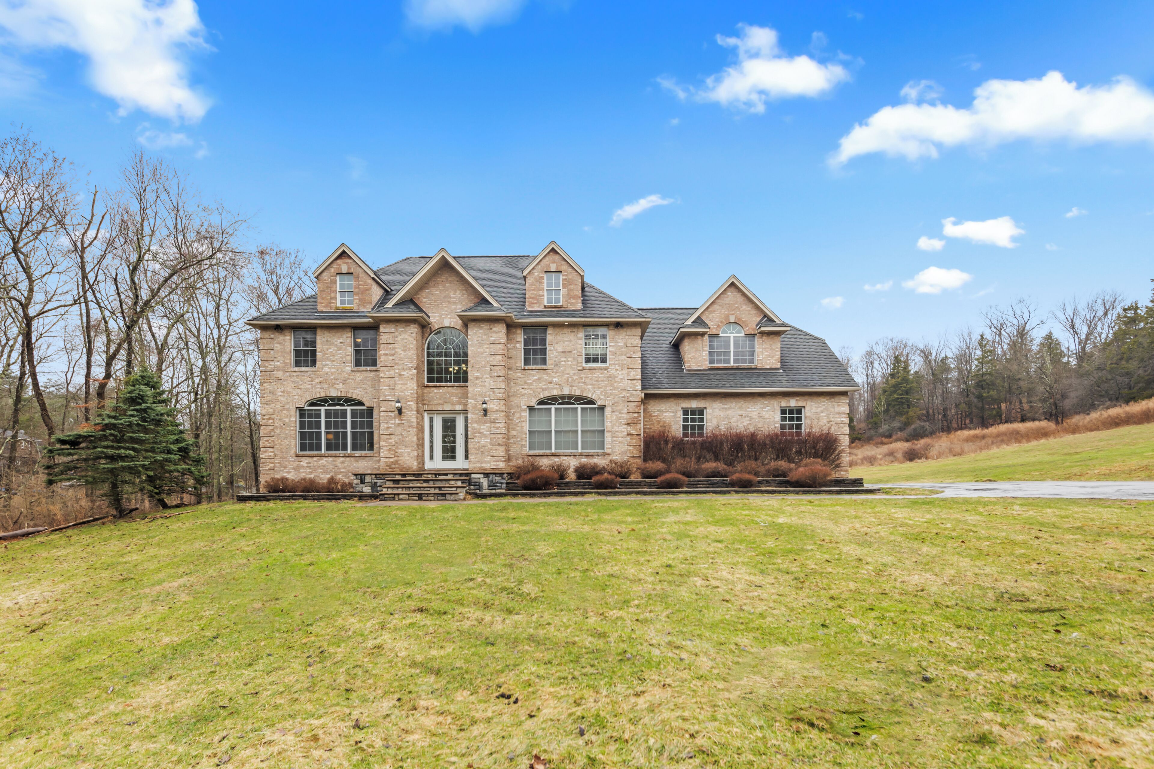 A large, two-story stone house with a prominent front entrance, multiple windows, and a well-maintained lawn.