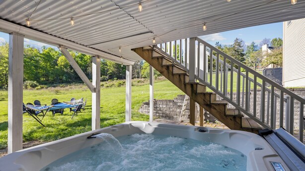 Un jacuzzi con muelle de madera y barandilla, rodeado de césped y un muro de piedra.
