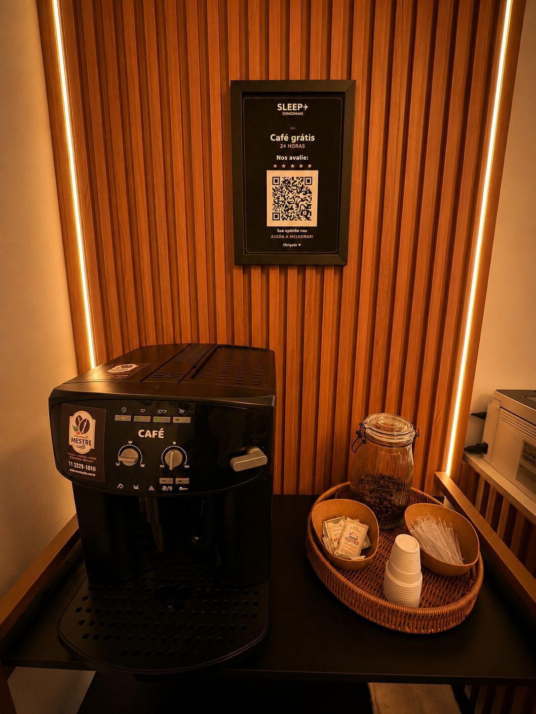 Une machine à café portant une étiquette de marque, un code QR pour recueillir les commentaires des utilisateurs, et un plateau avec des tasses à café et un bocal de grains de café.