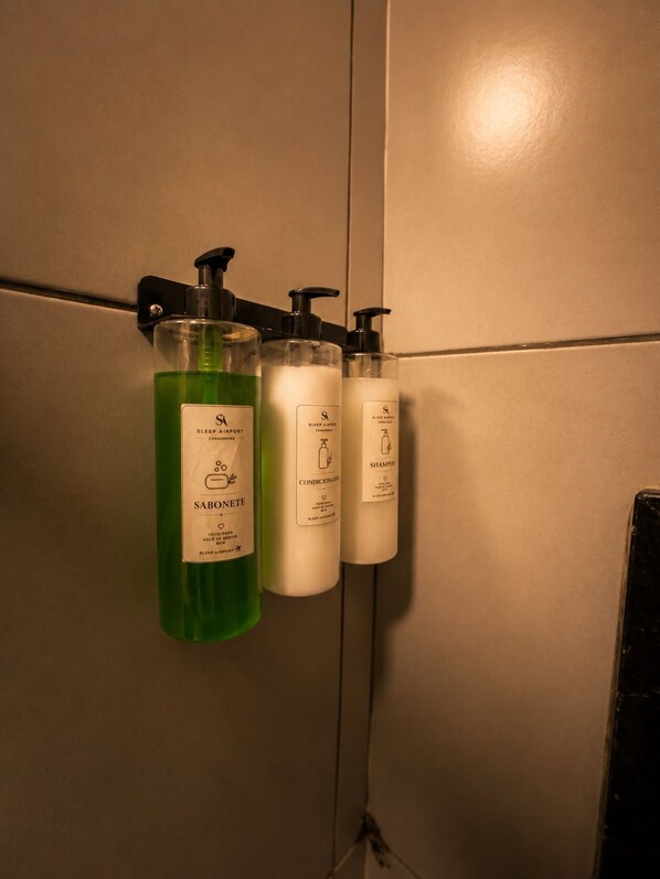 Trois produits de toilette fixés au mur, dont un savon liquide vert, un après-shampoing blanc et un flacon de shampoing blanc.