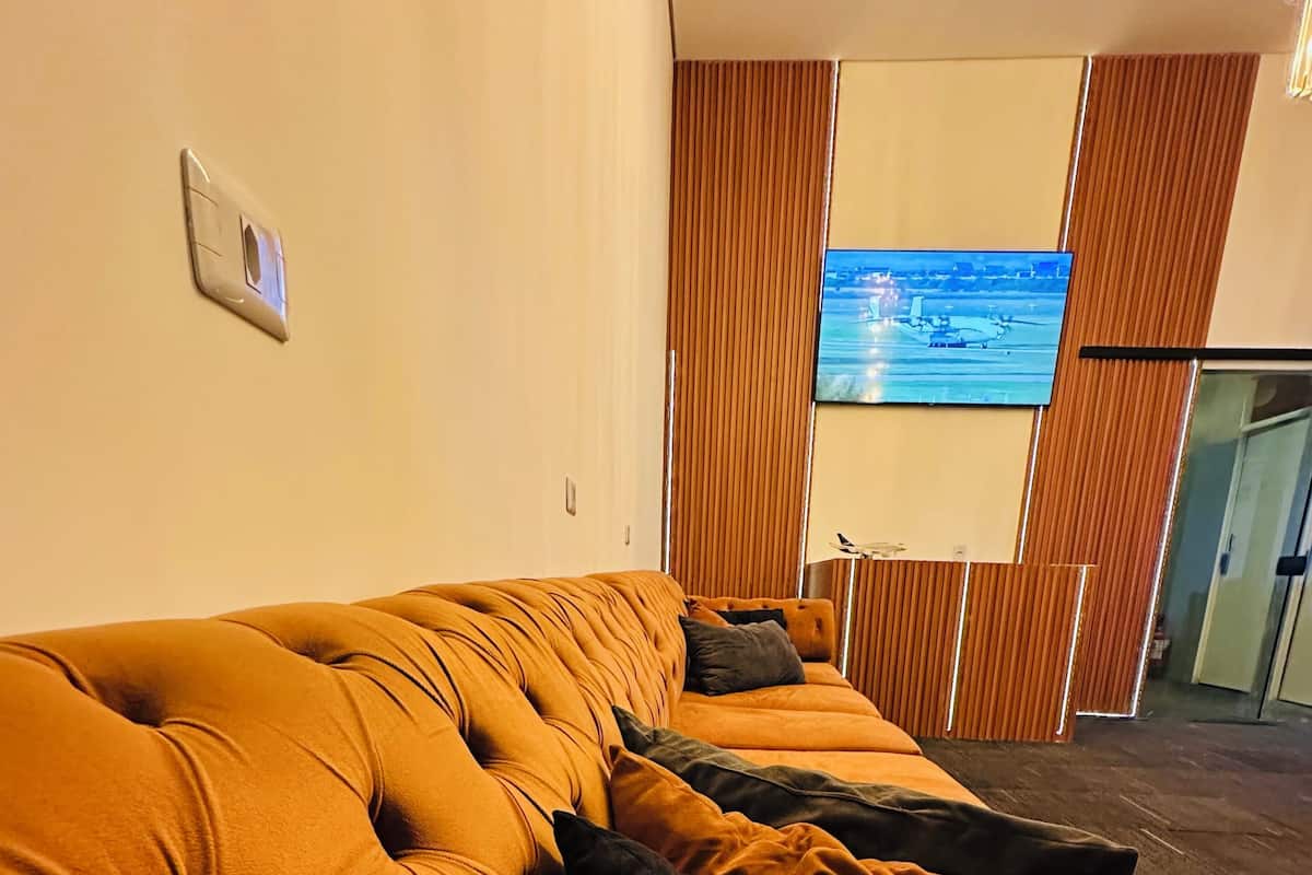 A modern living room with a large sofa, a flat-screen TV, and a view of the outdoors.