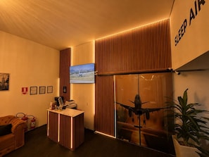 Een receptiezone met een receptiebalie, een aan de muur bevestigde televisie en een groot raam met uitzicht op een vliegtuig.
