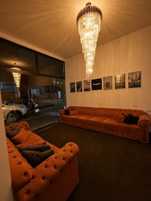 A modern living room with a large sofa, a smaller sofa, and a chandelier. There are framed pictures on the wall and a window with a view of the street. - Sleep airport congonhas (São Paulo)
