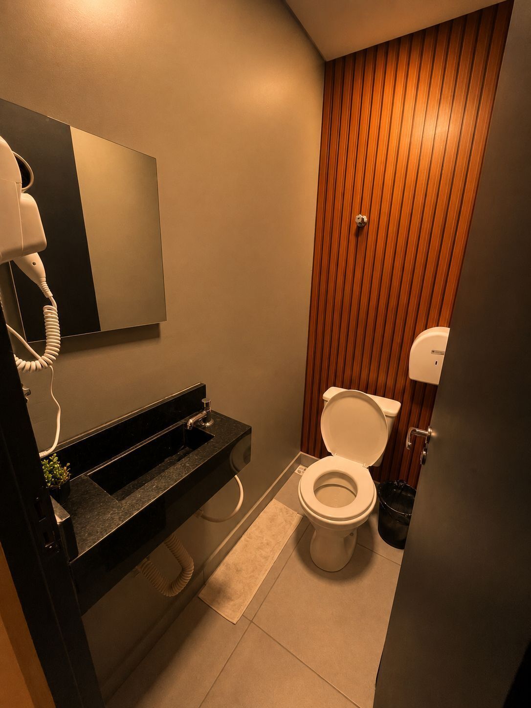 Un baño pequeño con inodoro, lavamanos con espejo y secador de pelo.