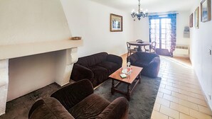 A living room with a fireplace, two sofas, a coffee table, and a dining table with chairs. - APPARTEMENT PROCHE PLAGE (Valras-Plage)