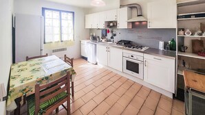 A kitchen with white cabinets, a stove, a sink, and a window with curtains. - APPARTEMENT PROCHE PLAGE (Valras-Plage)