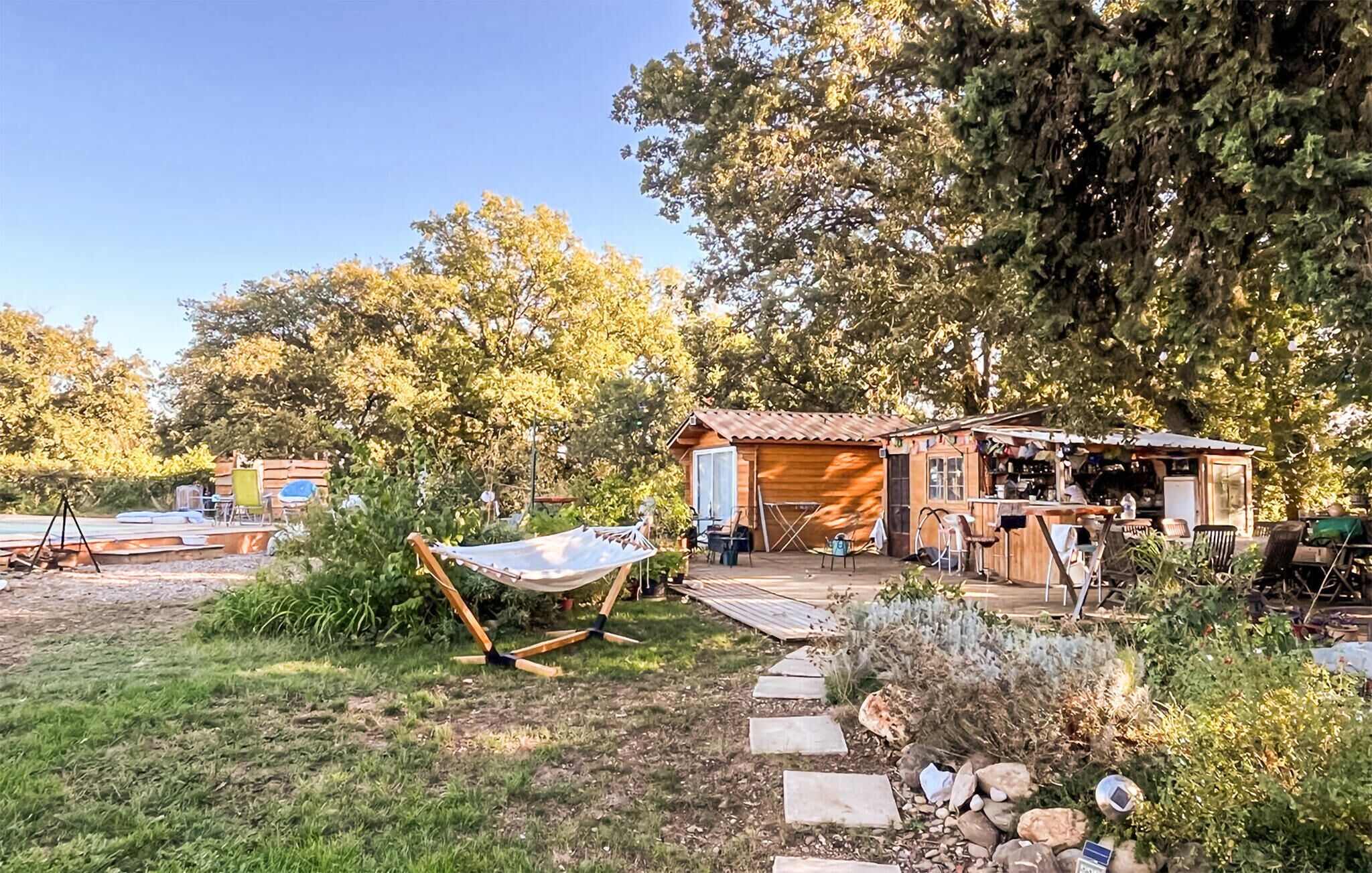 A rustic wooden cabin with a patio, surrounded by trees and a hammock.
