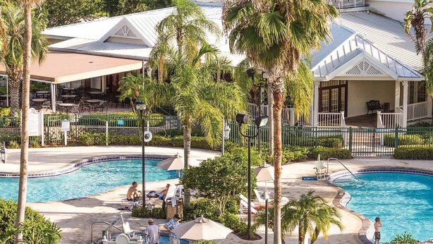A resort with two swimming pools, palm trees, and a covered outdoor seating area. - Worldmark Orlando Kingstown Reef Studio Deluxe (Orlando)