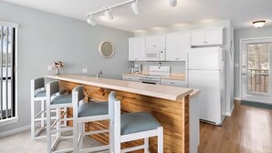 Una cocina moderna con armarios blancos, encimera de madera y barra integrada con tres taburetes.