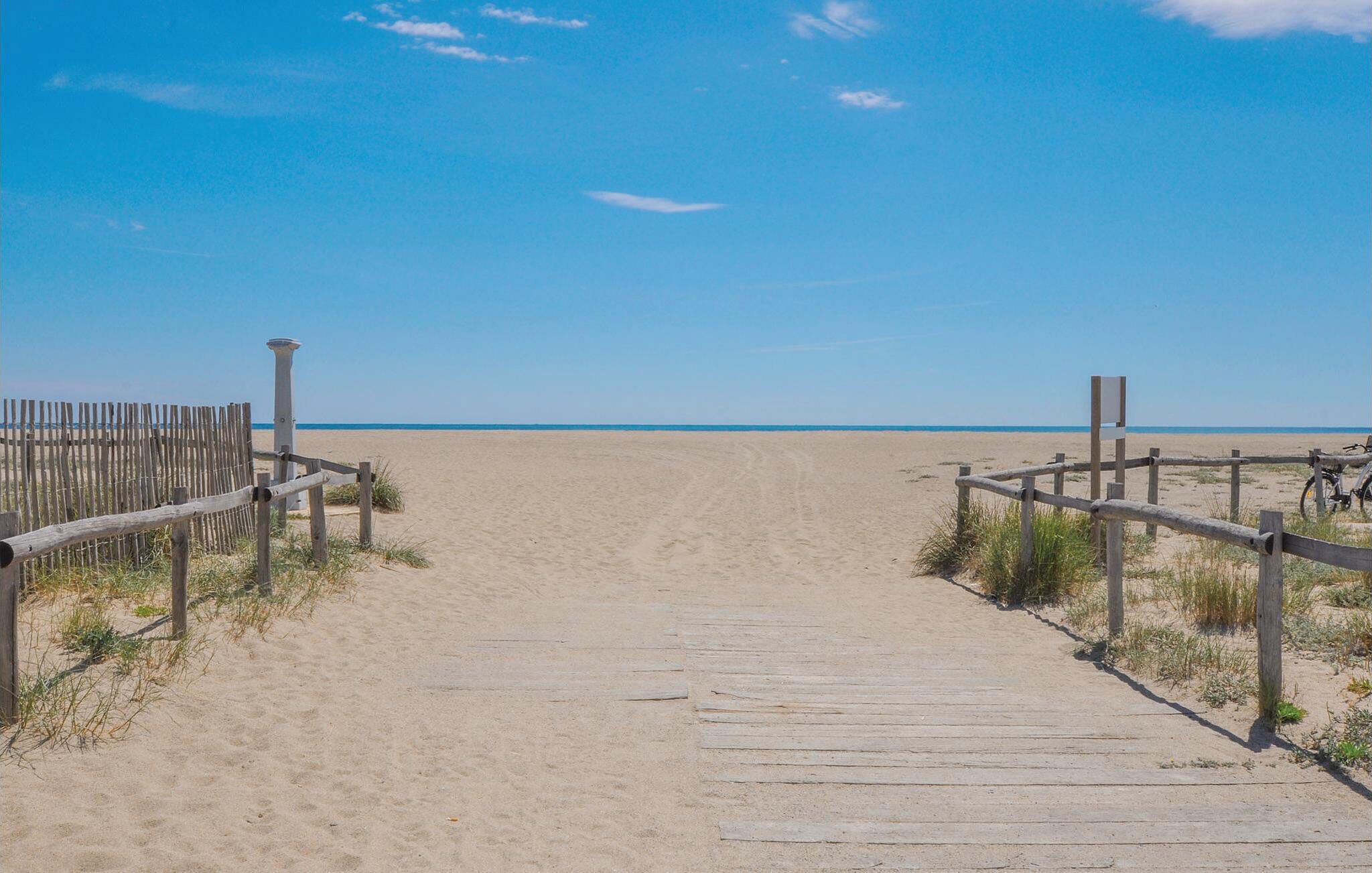 A wooden boardwalk leading to a sandy beach with a clear sky.