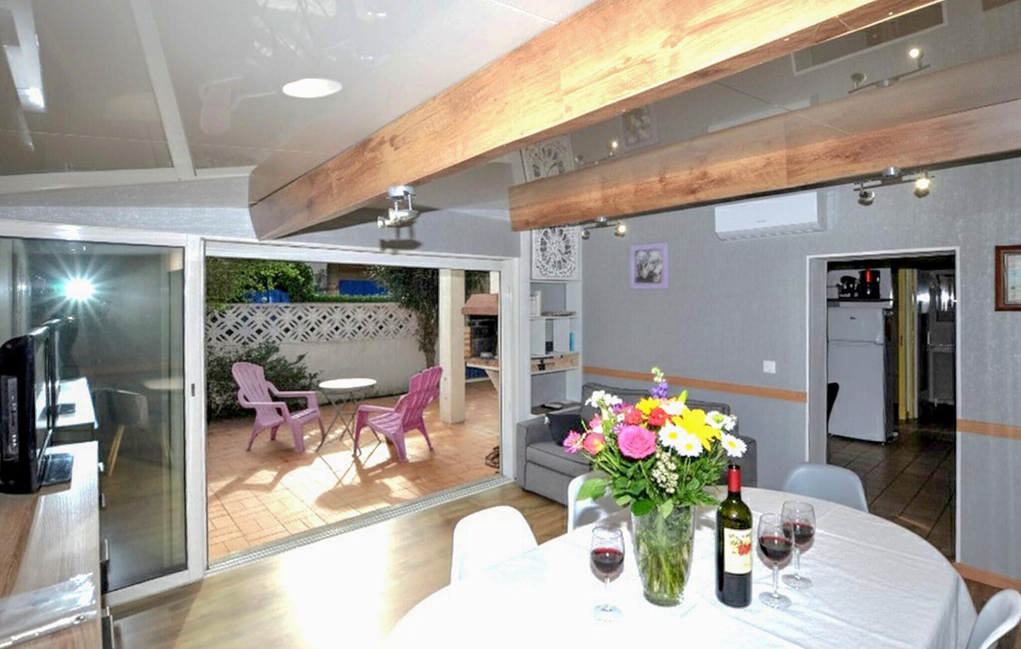A dining area with a table set for two, a vase of flowers, and a bottle of wine.