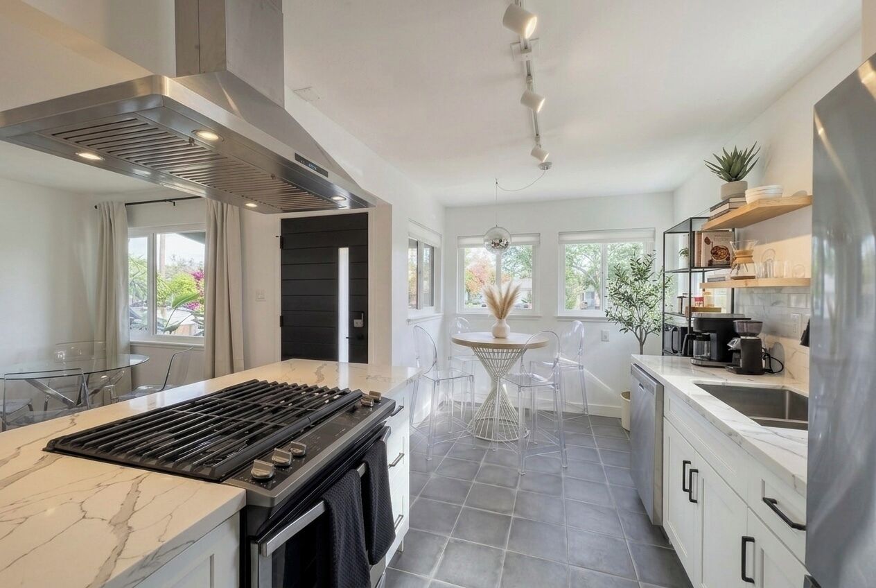 A modern kitchen with a gas stove, stainless steel appliances, and a dining area with a white table and chairs.