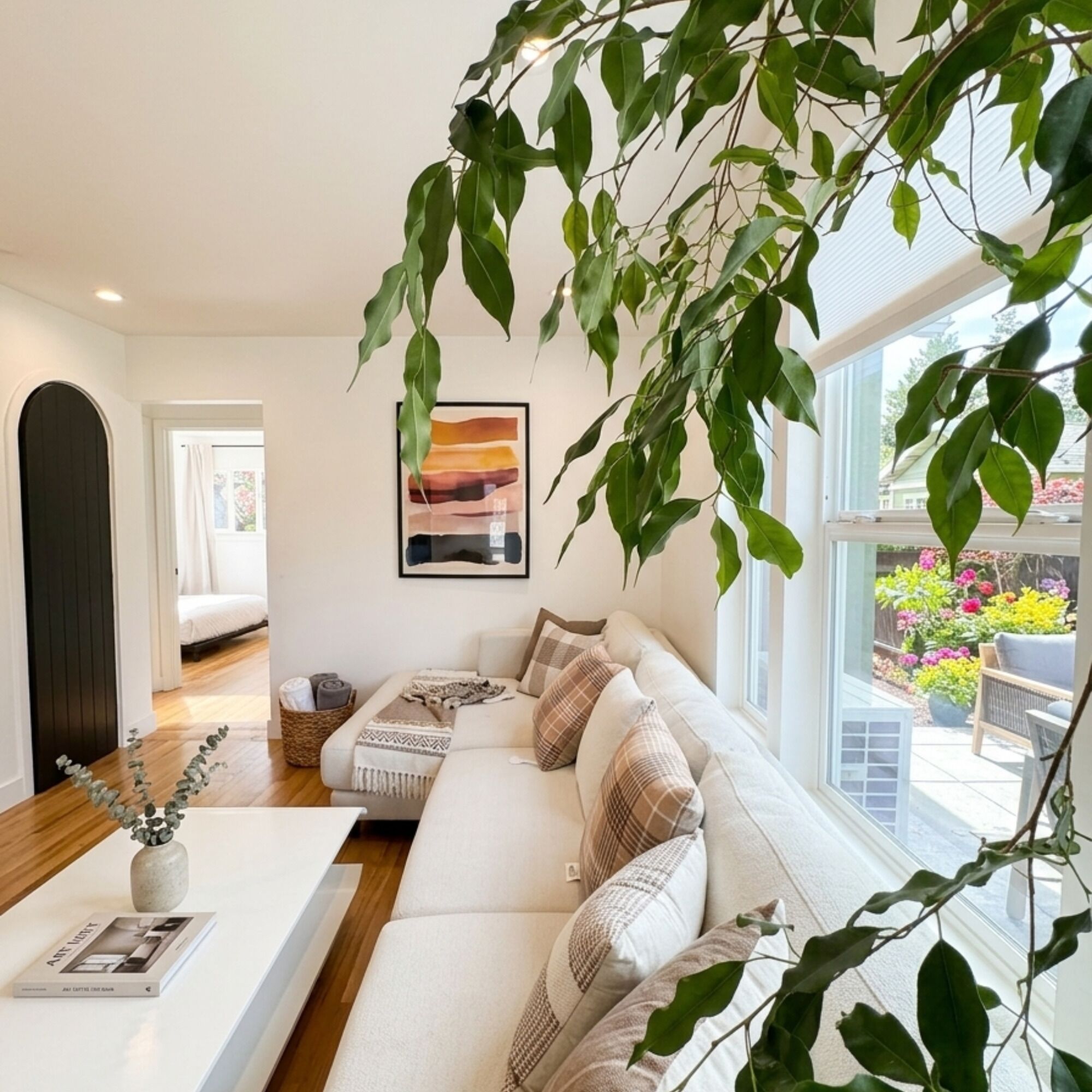 A modern living room with a white sofa, a coffee table, and a large window with a view of a garden.