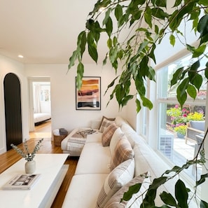 Ein modernes Wohnzimmer mit einem weißen Sofa, einem Couchtisch und einem großen Fenster mit Gartenblick.
