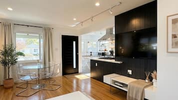 A modern living room with a glass table, a white sofa, and a flat-screen TV mounted on the wall.