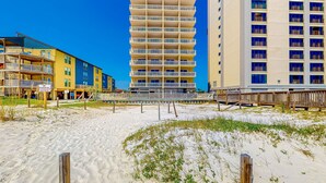 A beachfront hotel with multiple balconies, a sandy beach, and a wooden boardwalk. - Pet Friendly! Beach Front- East Corner Unit- 2 Pools- Caribbean 501 (Gulf Shores)