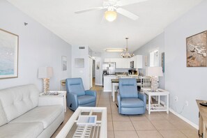 Ein modernes Wohnzimmer mit einem weißen Sofa, zwei blauen Sesseln, einem Couchtisch und einem Deckenventilator.