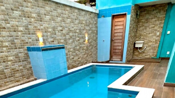 Une piscine avec un bord carrelé, un mur en briques et une porte en bois.