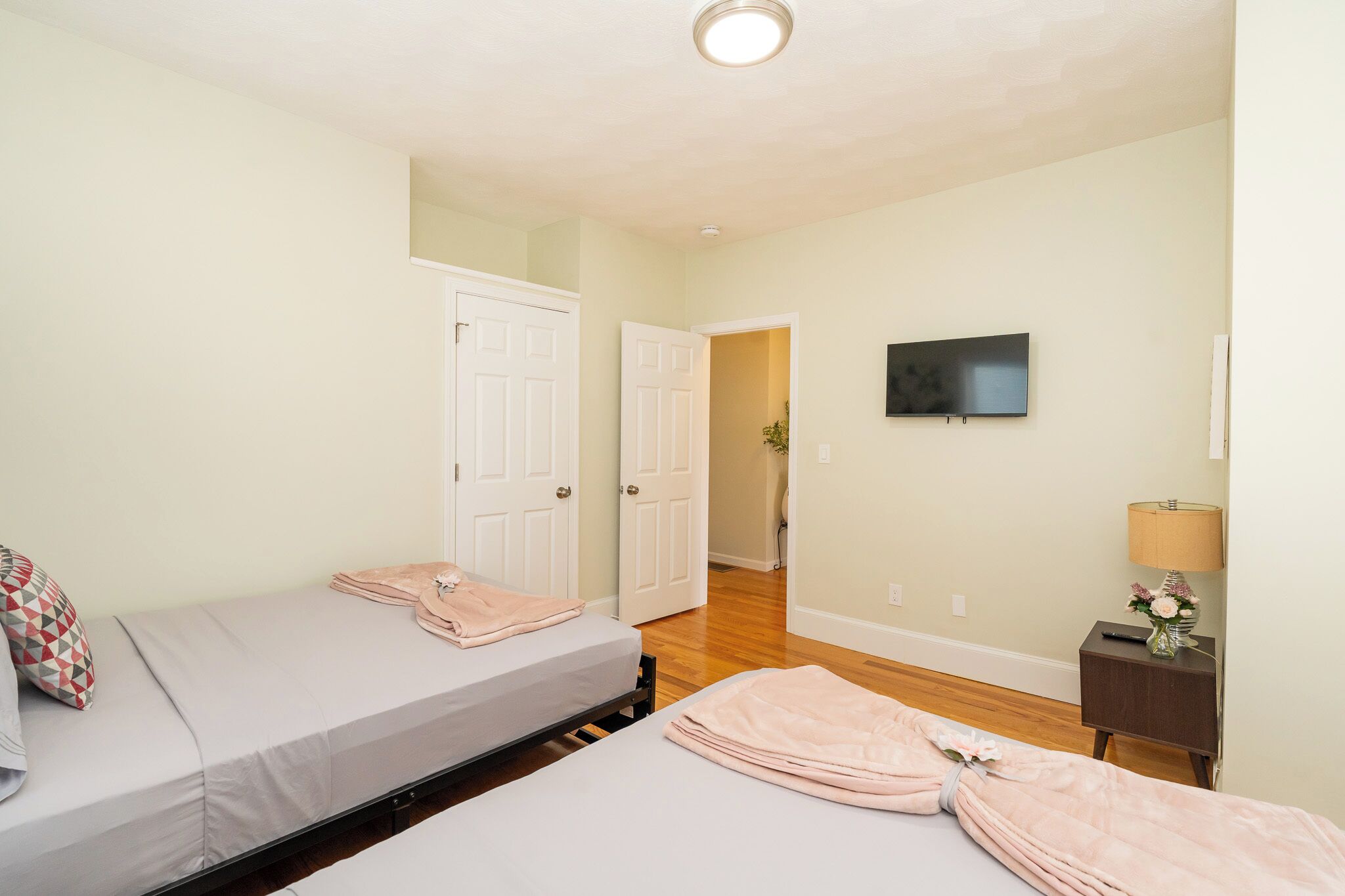 A bedroom with two beds, a TV, a lamp, and a door leading to another room.