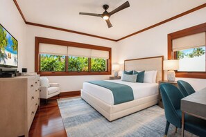 Ein Schlafzimmer mit einem Bett, einem Schreibtisch, einem Stuhl, einem Deckenventilator und einem Fenster mit Blick ins Grüne.