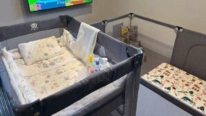 Un berceau pour bébé avec un matelas à motifs, une petite table sur laquelle se trouve un biberon, et un téléviseur diffusant un dessin animé.