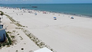 Ein Strand mit blauem Himmel, einem Pier in der Ferne und einigen Personen.