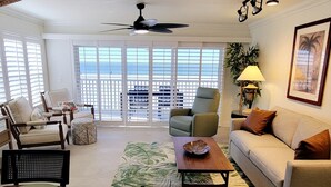 Ein Wohnzimmer mit Essbereich, Deckenventilator, einer Couch, einem Couchtisch und Blick durch große Fenster.