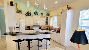 A modern kitchen with white cabinets, a central island with bar stools, a microwave, and a coffee machine. - !Fun for Families! Large Pool Home + Game Room! (Fort Myers Beach)