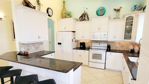 A kitchen with white cabinets, a central island with bar stools, a microwave, oven, and a refrigerator. - !Fun for Families! Large Pool Home + Game Room! (Fort Myers Beach)