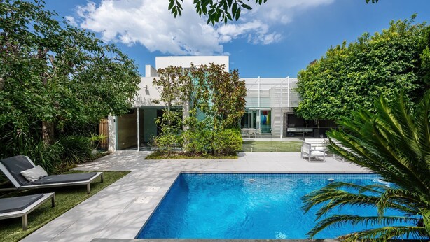 A modern outdoor pool area with lounge chairs, a clear blue pool, and lush greenery. - The Art House by the Beach (Brighton)