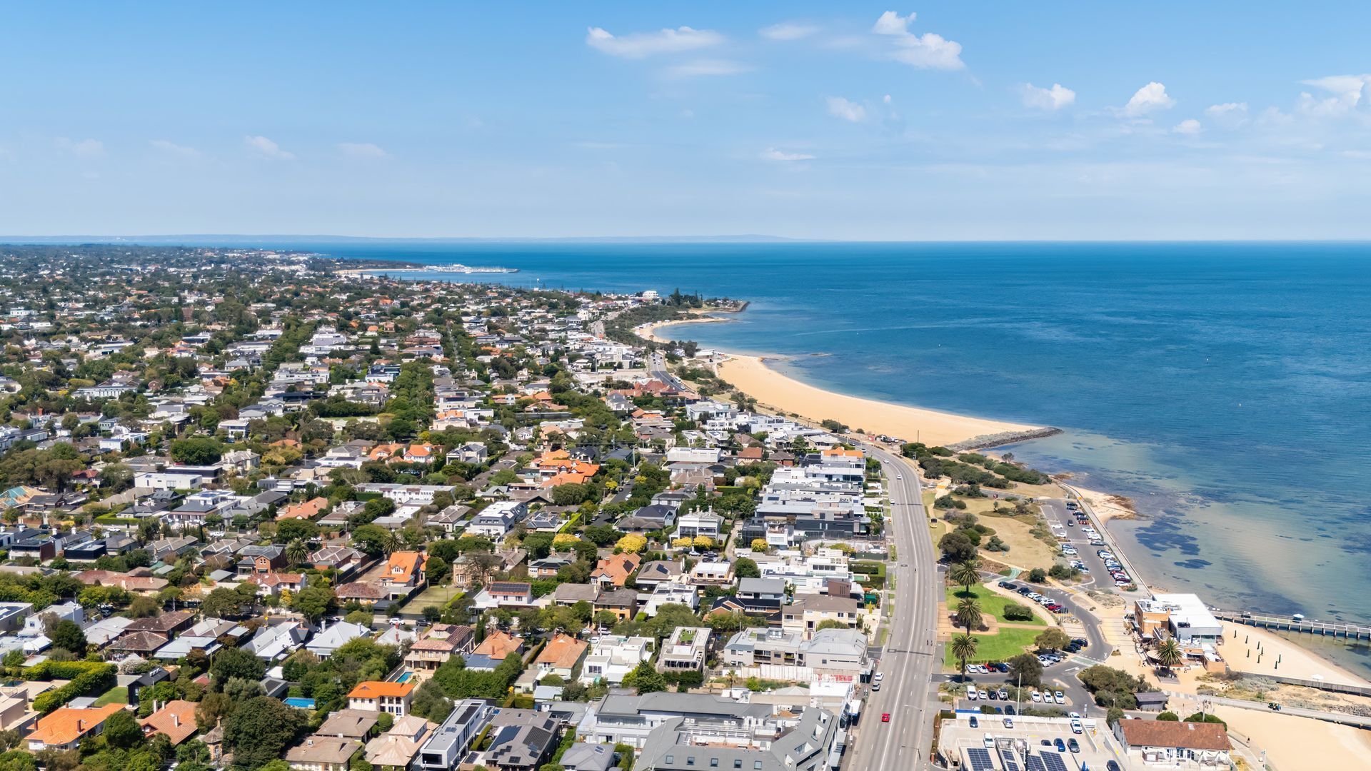 An aerial view of a coastal residential area with houses, a beach, and a road leading to the shore.