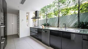 A modern kitchen with a stainless steel sink, black cabinetry, and a view of a green tree outside. - The Art House by the Beach (Brighton)