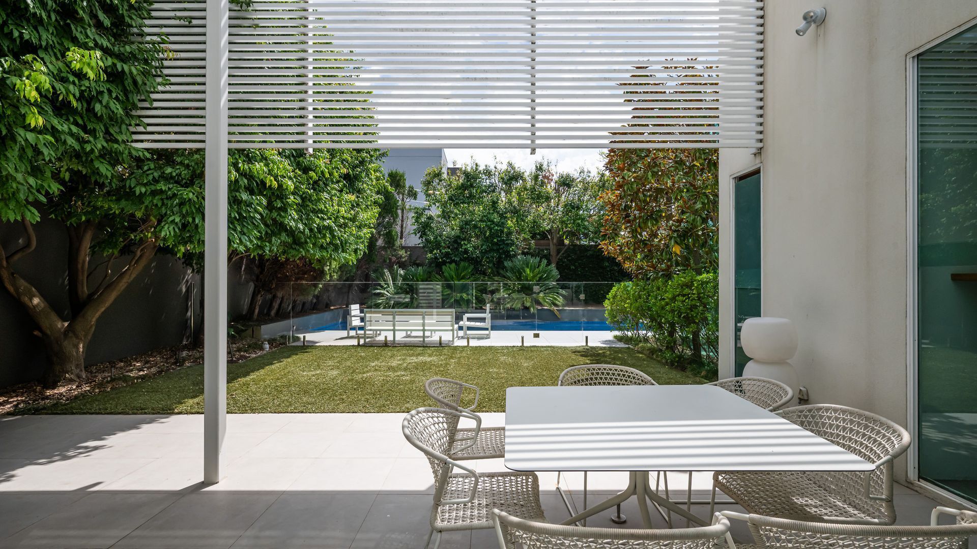 A patio with a table and chairs, a swimming pool, and a view of a garden.