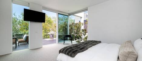 Une chambre moderne dotée d’un grand lit, d’un téléviseur à écran plat fixé au mur et d’une porte-fenêtre coulissante donnant sur une terrasse extérieure.