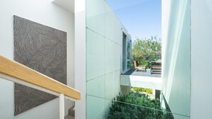 A modern interior with a staircase, a geometric wall art piece, and a glass railing overlooking a garden. - The Art House by the Beach (Brighton)