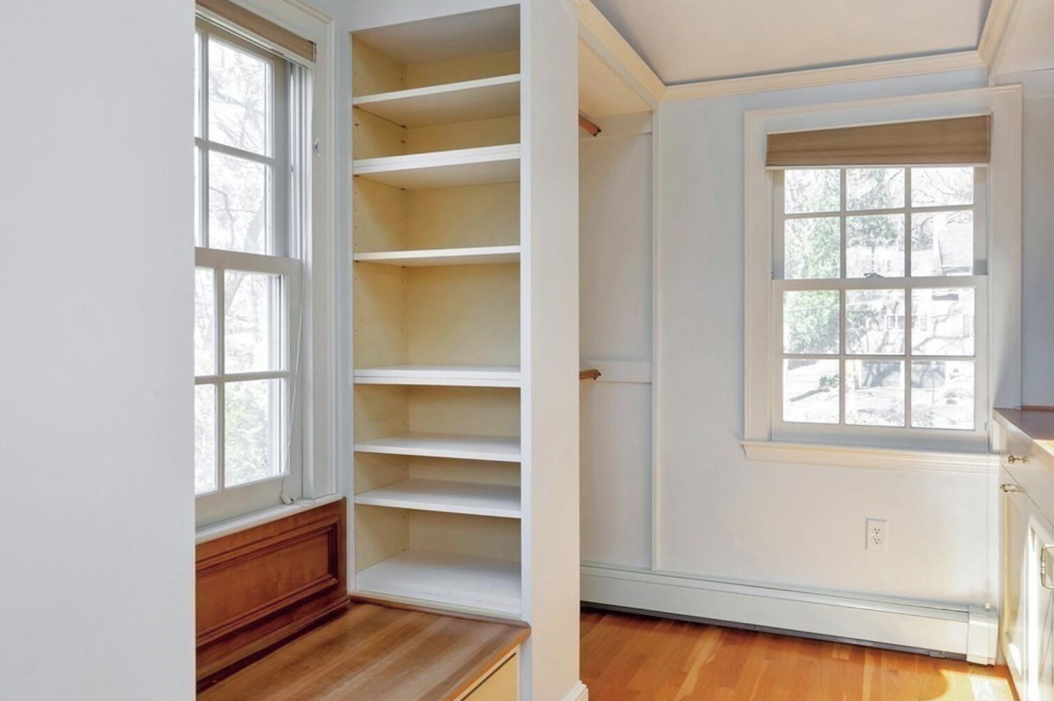 Ein Zimmer mit großem Fenster, eingebauten Regalen und Holzboden.
