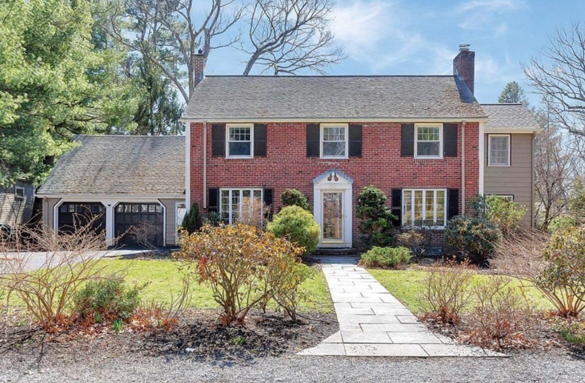 A two-story brick house with a front entrance, a covered garage, and a well-maintained lawn.