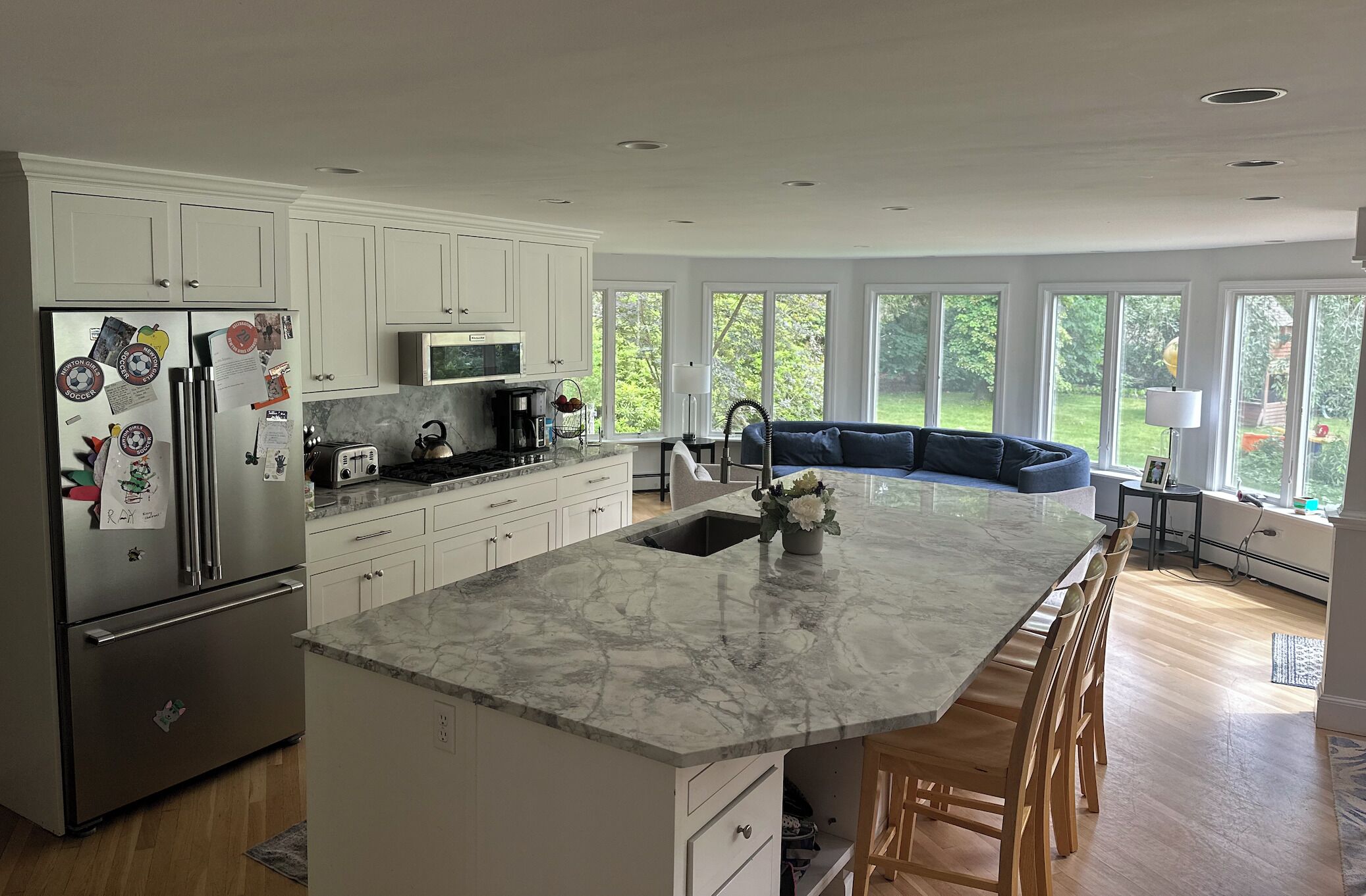 A modern kitchen with a marble island, white cabinetry, stainless steel appliances, and a large window overlooking a green landscape.