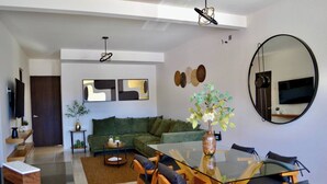 A modern living room with a glass dining table, green sofa, and a large mirror. - Encanto Department We Bill (San Miguel de Allende)