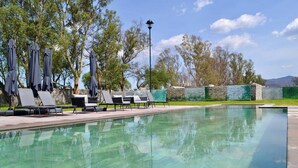 A swimming pool with lounge chairs and umbrellas, surrounded by stone walls and trees. - Encanto Department We Bill (San Miguel de Allende)