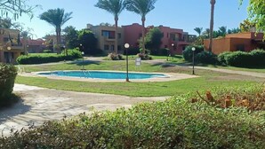 Ein Pool, umgeben von Grünflächen, Palmen und Gebäuden mit Balkonen.