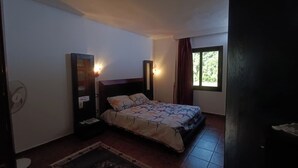 Ein Schlafzimmer mit einem Bett, zwei Wandlampen, einem Vorhangfenster, einem Ventilator und einem kleinen Tisch.