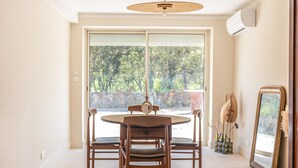 Zona pranzo con tavolo rotondo e sedie, una grande finestra con vista sugli alberi e una ventola a soffitto.