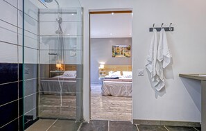 A modern bathroom with a glass shower enclosure, a visible bed with white bedding, and a towel rack with towels. - Beautiful home in Berrias et Casteljau (Berrias et Casteljau)
