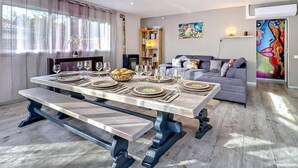 En matplats med ett stort bord dukat för en måltid, en soffa och en bokhylla i ett modernt vardagsrum.