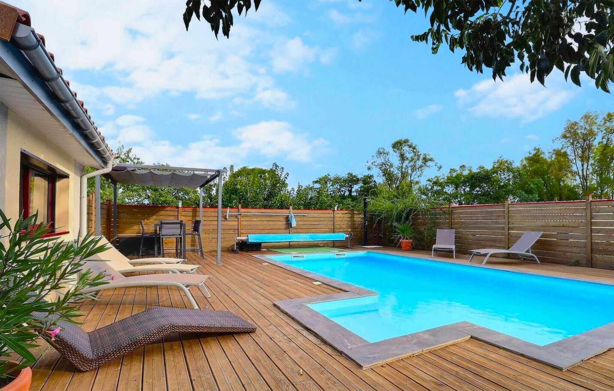 Patio trasero con piscina, terraza de madera, sillas de descanso y un área de patio cubierta.