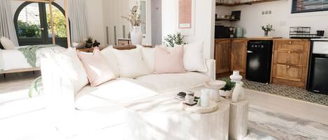 Ein modernes Wohnzimmer mit einem weißen Sofa, einem Couchtisch und einer Küchenzeile mit Holzausbau und einem schwarzen Geschirrspüler.