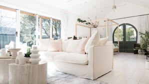 Een ruime woonkamer met een witte bank, een houten salontafel en een groot raam met uitzicht op de omgeving.