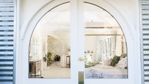 A white arched door with a view into a room with a bed, a desk, and a plant.