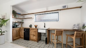 A compact kitchen with wooden cabinets, a black dishwasher, a white sink, and a window with blinds.